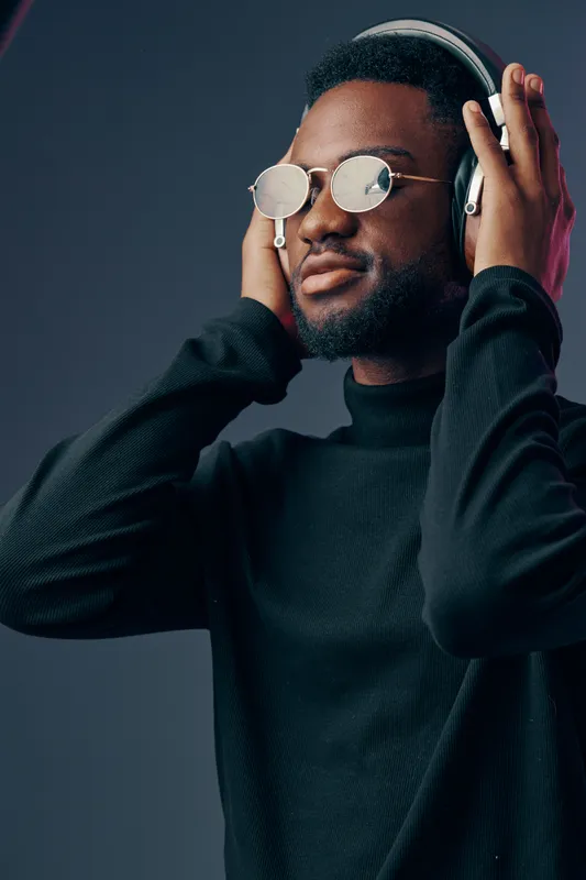 Stylish Black man wearing headphones and sunglasses, enjoying music, against a gradient background with vibrant hues, perfect for lifestyle and entertainment themes