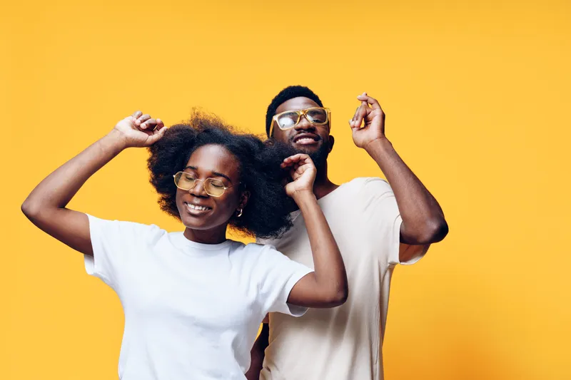 Joyful young couple dancing together against a vibrant yellow background, showcasing happiness and connection with lively expressions and casual attire