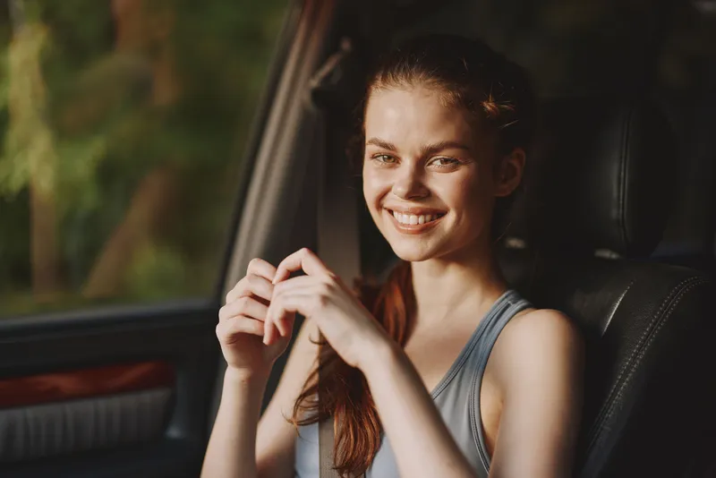 Young woman with a joyful expression in a car, wearing casual clothing, surrounded by a natural background, perfect for travel and lifestyle themes