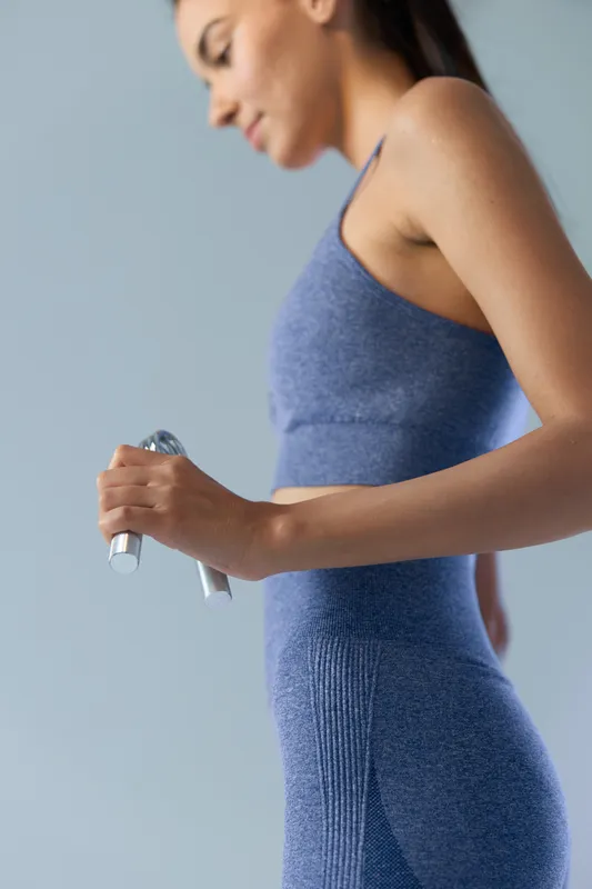 Woman sport fitness holding dumbbell in blue workout clothes, showing focused determination and healthy lifestyle against a soft light background, fitness concept.