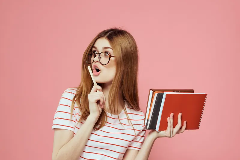 Молодая студентка с книгами на розовом фоне, в очках