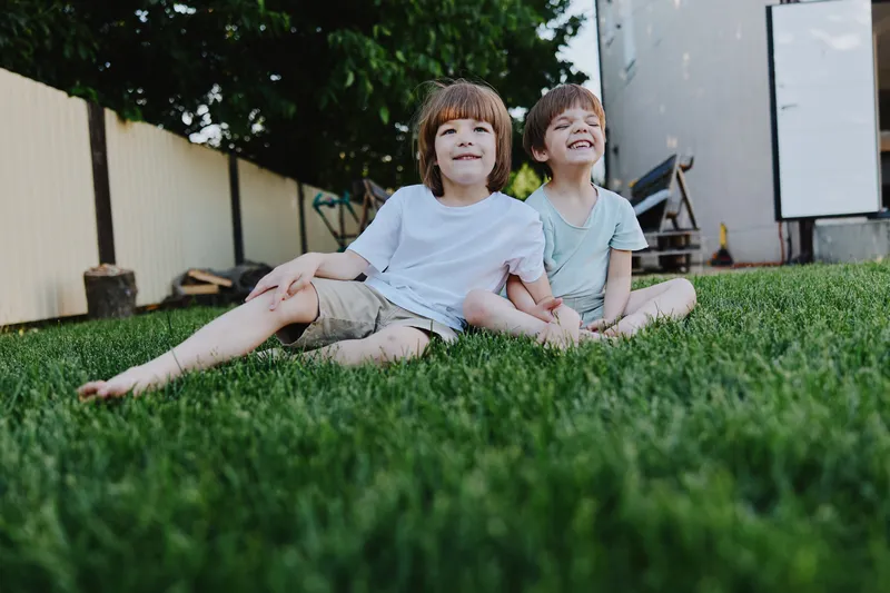 Happy children sitting on green grass, enjoying a sunny day outdoors with smiles on their faces, conveying a sense of joy and friendship in a playful setting.