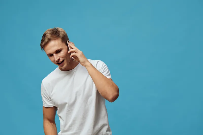 smiling young caucasian man talking on smartphone wear white t-shirt isolated blue background digital nomad communication concept