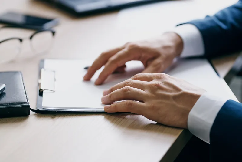 Бородатый мужчина сидит за столом перед ноутбуком, похожий на финансового работника