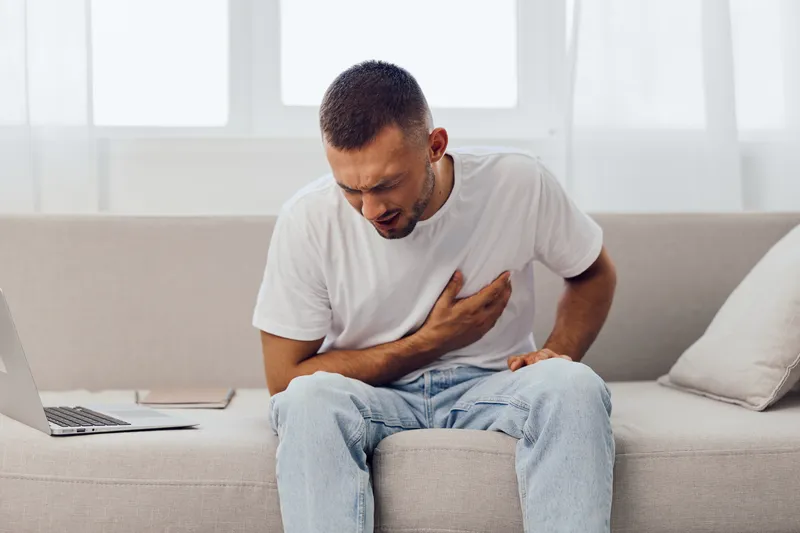 Man sitting on a couch, experiencing anxiety and emotional stress, reflecting on modern life's challenges, highlighting burnout and mental health awareness.