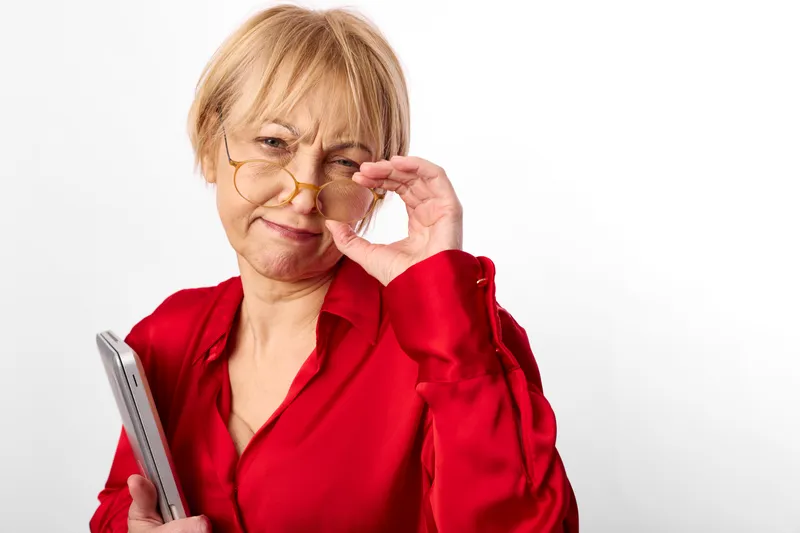Woman with glasses smiling applies face cream using a cotton pad for skincare wellness, close up on white background, red blouse, soft studio light, self care