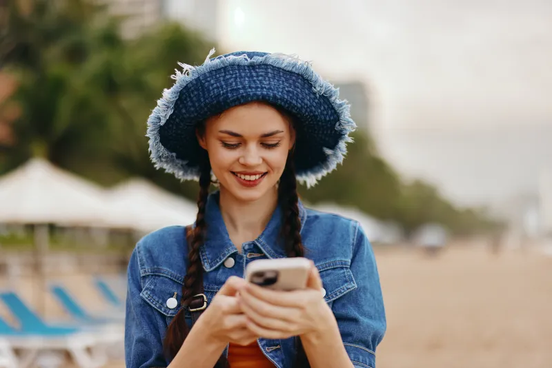 Счастливая молодая женщина пользуется смартфоном на улице в осеннем городском парке