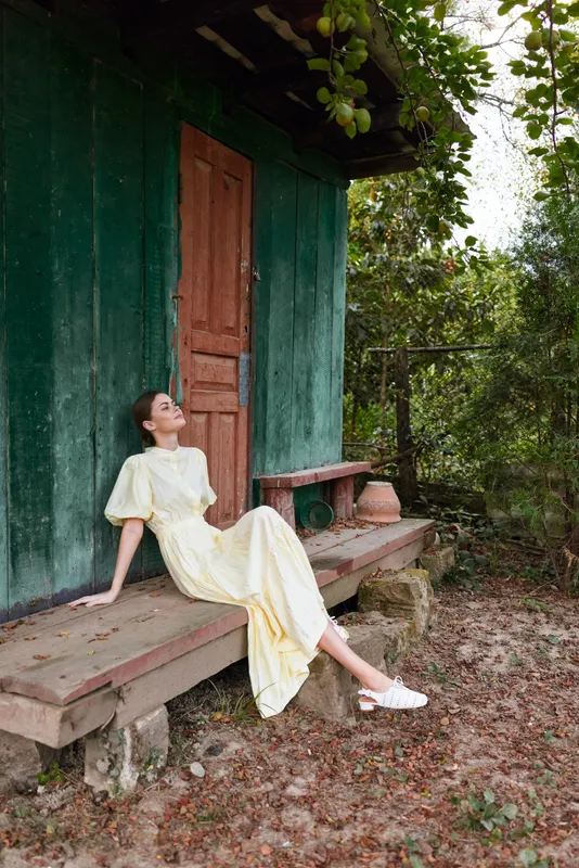 woman in yellow dress sitting on wooden bench at rustic cottage rural nature with relaxed mood authenticity inclusivity