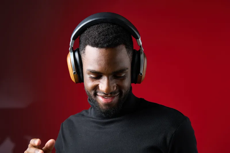 Happy young man enjoying music with modern headphones, smiling against a red background, conveying joy and relaxation in a contemporary setting