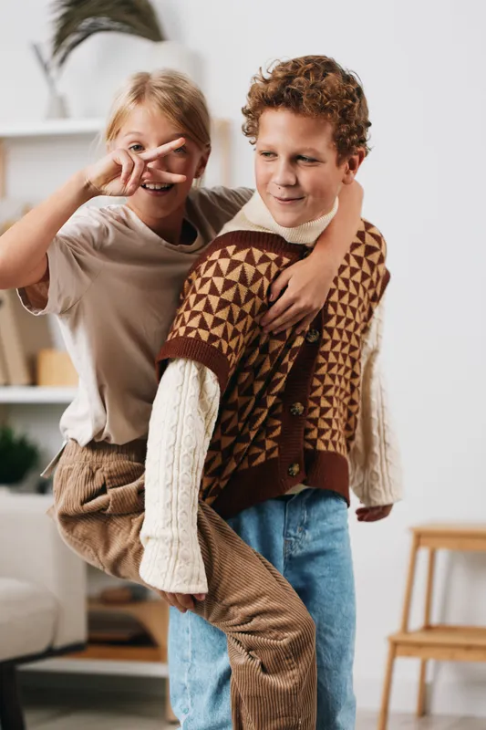 Playful piggyback moment between two friends indoors, capturing joyful laughter, cozy outfits, and a warm sense of companionship in a bright, homey setting.
