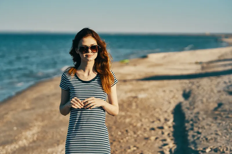 Красивая женщина в футболке и очках на пляже у моря в горах