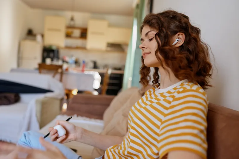 Calm woman with wavy hair applying lotion at home, seated on a sofa, warm ambient lighting, casual self care and skincare routine in a cozy living space