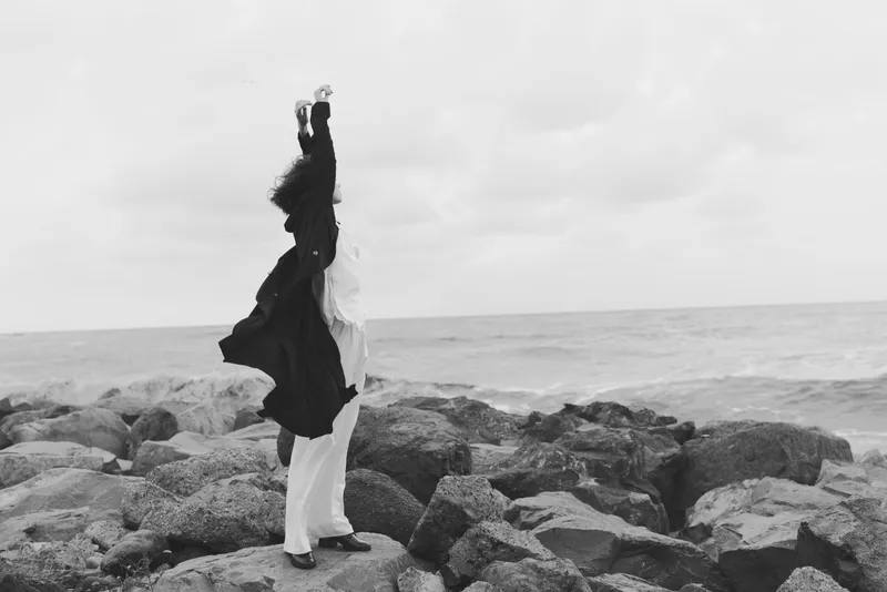 Couple dancing on rock shore by the sea in wedding attire, silhouette against a gray sky, celebration and romance beside the waves