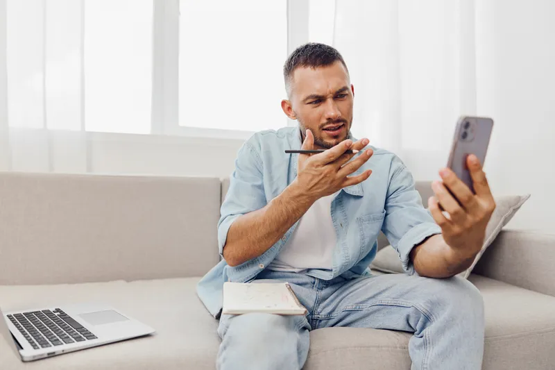 Concerned man looking at his smartphone while thinking deeply, casual outfit in a cozy living room, modern decor, warm colors, digital lifestyle.