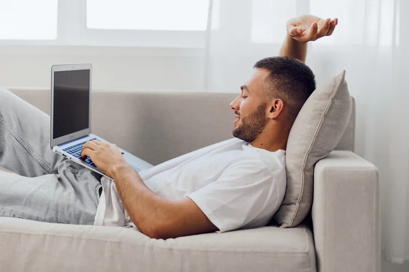 Relaxed man working on a laptop at home, showcasing a modern lifestyle with cozy interiors and a sense of comfort and productivity in a serene environment.