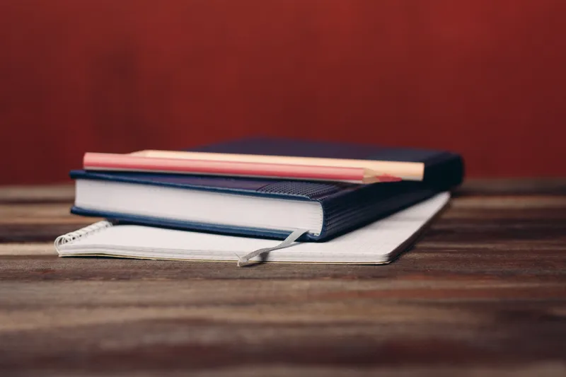 Книга с блокнотом, карандаши, офисные документы и предметы на деревянном столе