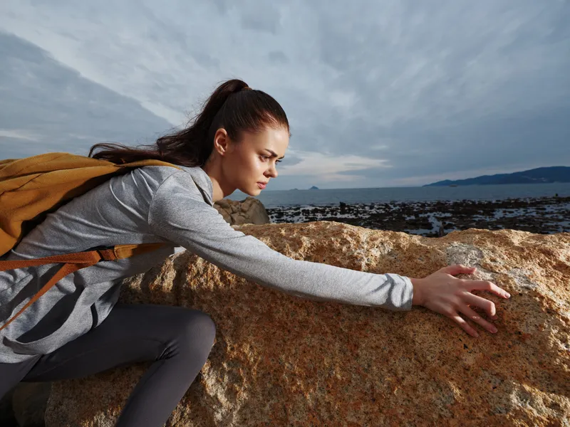 Young woman climbing on a rocky coast, wearing activewear, demonstrating determination and focus in outdoor adventure setting