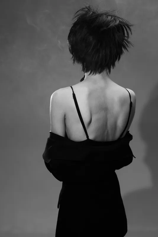 Black and white artistic portrait of a slender woman with short hair and exposed back in a dark outfit.