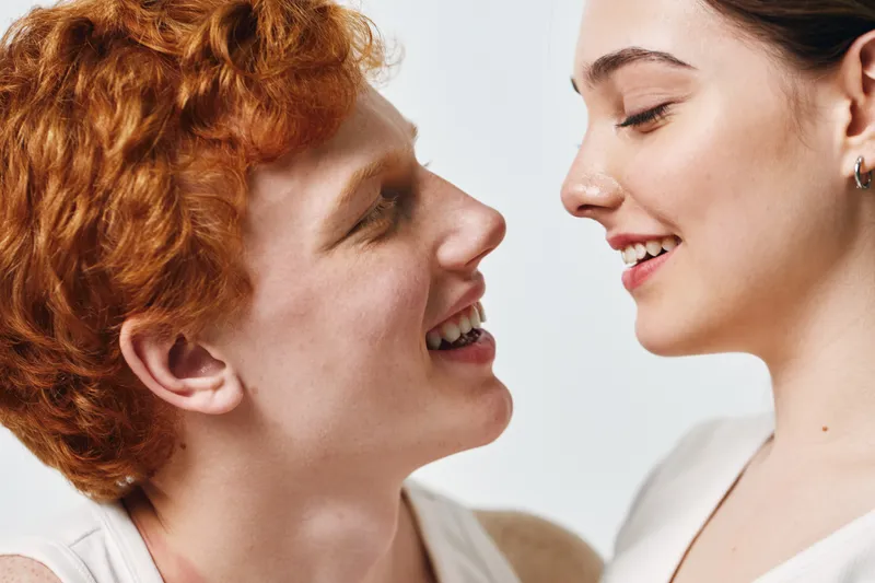 Young couple closeup, man with red hair and woman smiling face, looking at each other with joy and connection. Intimate moment, happiness and love between diverse partners.