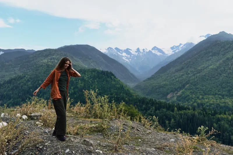 Woman hiking along a rocky ridge in a vast mountain landscape, wearing a jacket and exploring a breathtaking outdoor scene with misty valleys.