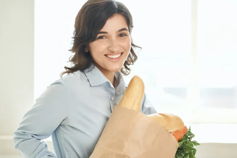 Женщина в семейных футболках держит пакет с продуктами, символизируя здоровое питание и домашние дела