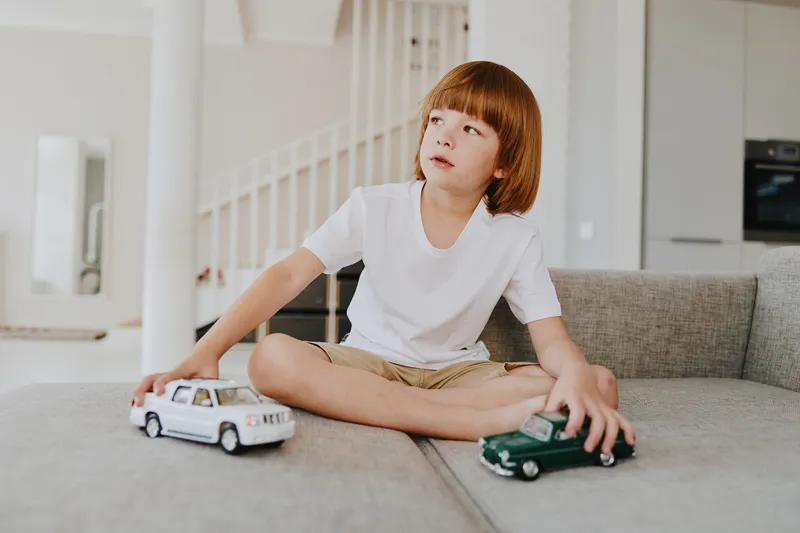 A thoughtful boy playing with toy cars, showcasing creativity and imagination in a bright, modern living space filled with natural light.