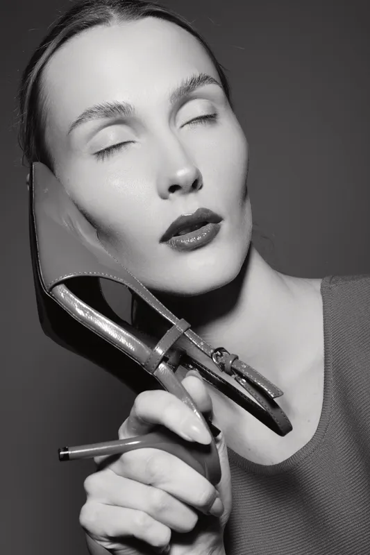 Close-up portrait of a fair skinned European woman with closed eyes holding a high heel shoe to her face. Artistic black and white fashion concept with elegant mood and makeup.