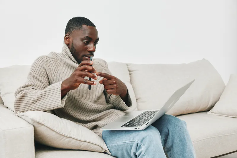 Young Black man engaging in a video call while sitting on a cozy sofa, wearing a stylish knitted sweater and expressing enthusiasm