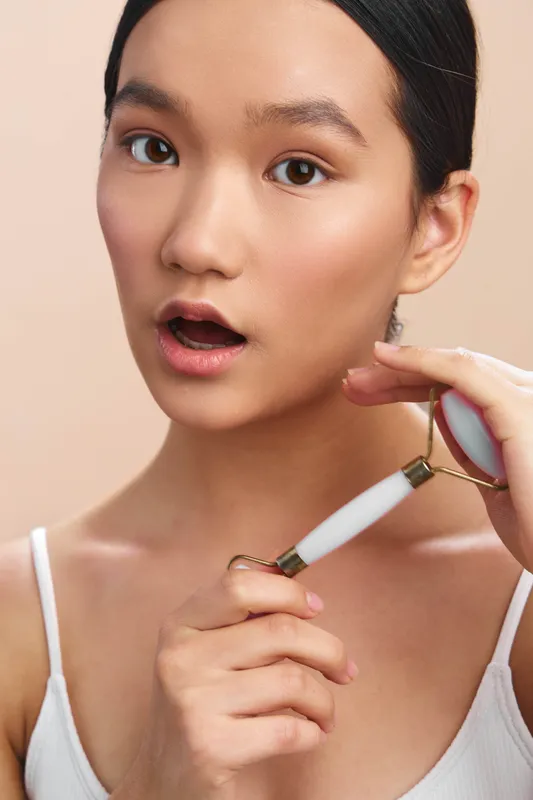 asian woman applying a facial device to her cheek in a clean studio, close up portrait with calm focus, soft lighting, and subtle glow, capturing a modern beauty routine moment.