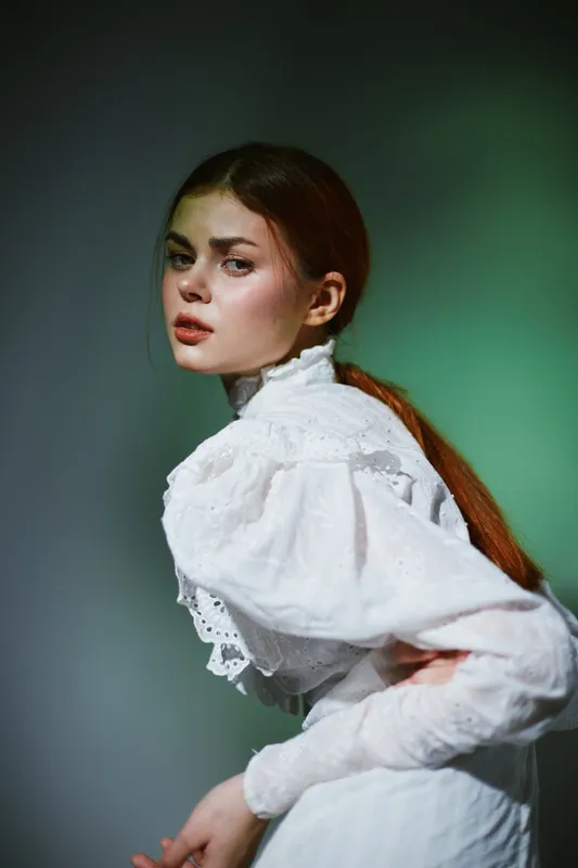Young woman in elegant vintage dress, showcasing emotion with soft lighting and a blurred green background, conveying a sense of nostalgia and grace