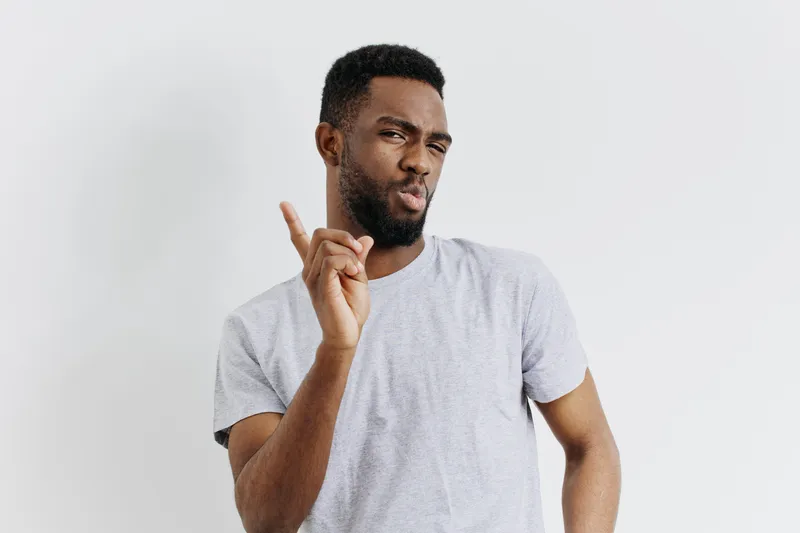 Уверенный молодой афроамериканец улыбается и показывает жест «окей» на нейтральном фоне, символизируя позитив и одобрение