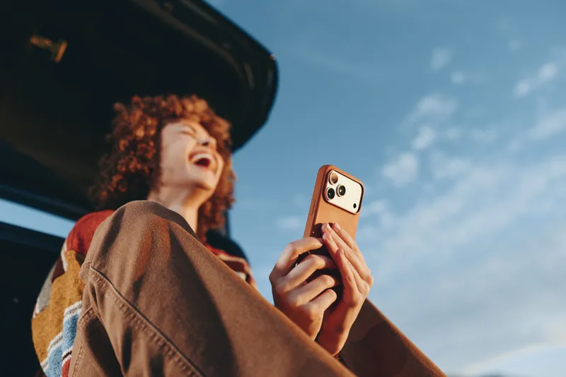 Woman selfie smartphone lifestyle outdoors sky curly hair casual portrait, smartphone in hand, natural daylight, looking up near car window, candid travel moment with smile
