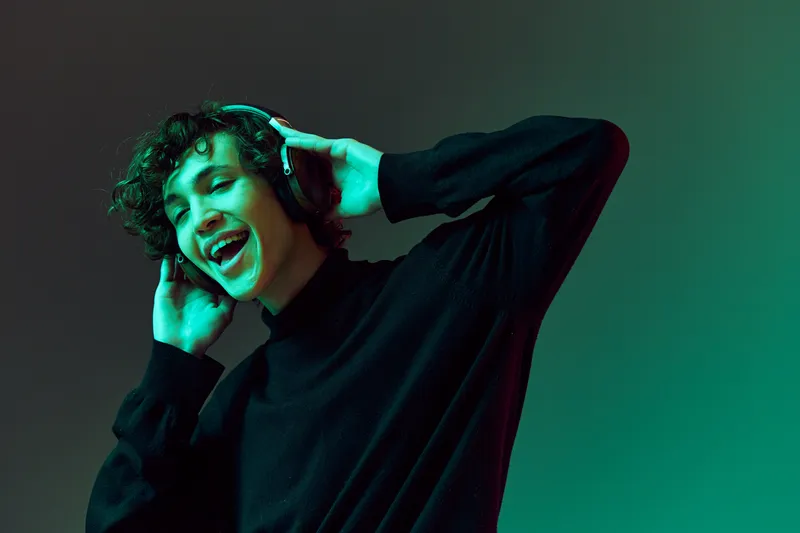 Мужчина в наушниках слушает музыку и танцует, DJ, счастье и улыбка, смех, образ жизни хипстера-подростка, портрет на зеленом фоне со смешанным неоновым светом, свободное пространство для копирования