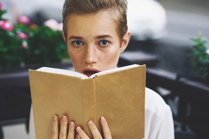 Студент с книгой в руках читает на прогулке на свежем воздухе, образование