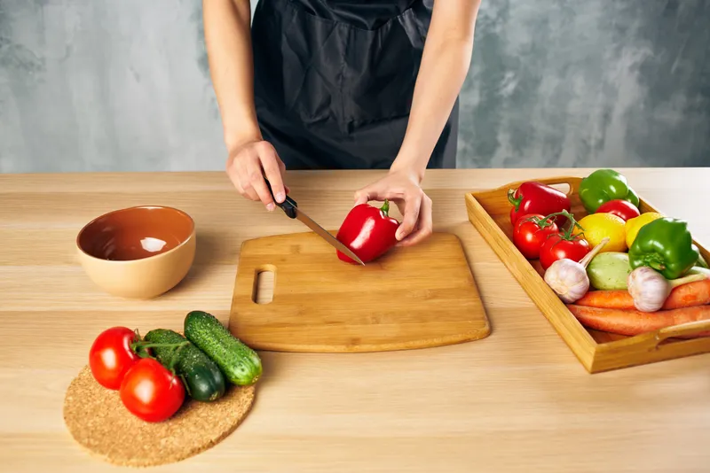 Женщина в черном фартуке на кухне нарезает овощи