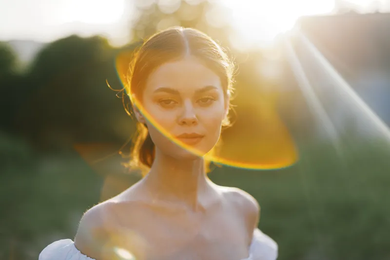 Beautiful young woman in soft sunlight with natural makeup, wearing an elegant white dress, evoking a serene and dreamy atmosphere in nature