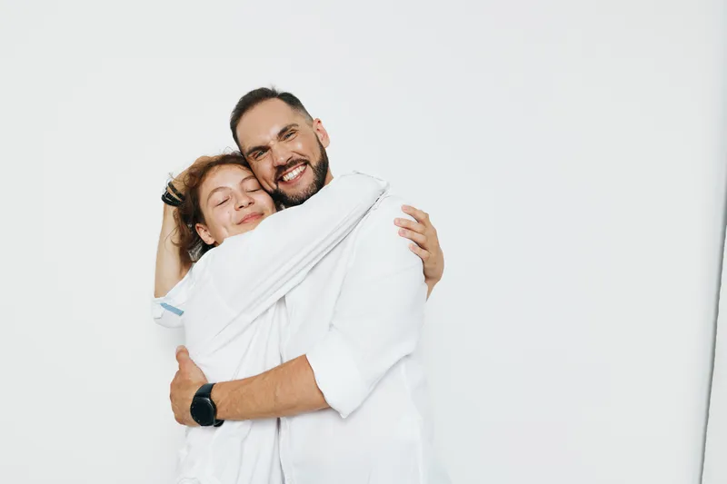 A professional man in a business setting, smiling with confidence, against an isolated colored background, communicates success, leadership, and warm teamwork through a friendly, engaging hug.