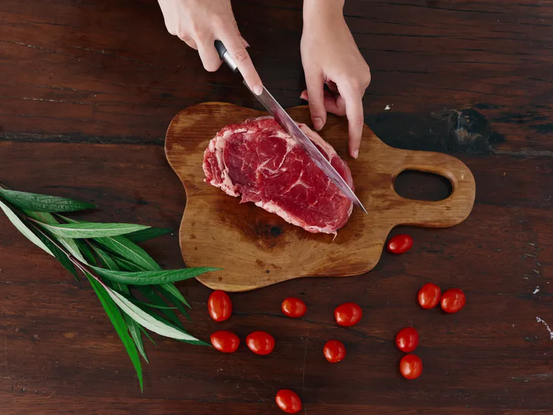 Женщина с ножом в руке нарезает свежее мясо для стейка, которое будет запекаться на кухне
