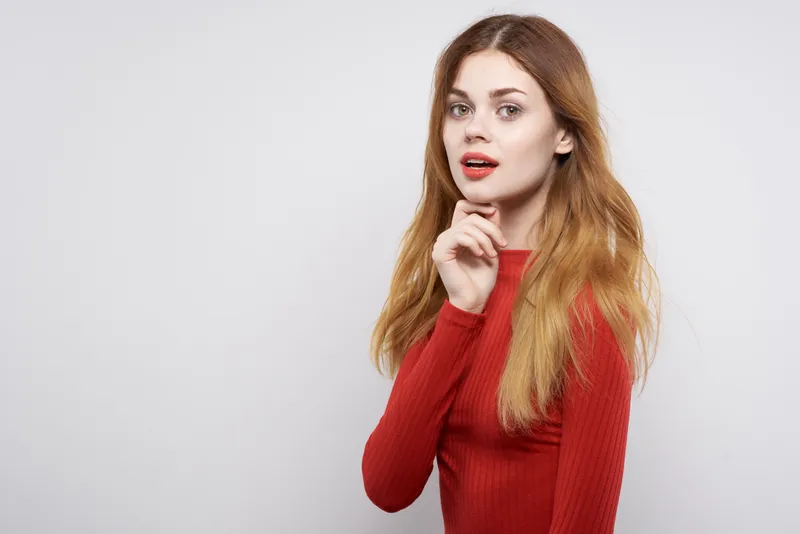 Привлекательная женщина в красном свитере с модной прической позирует на изолированном фоне