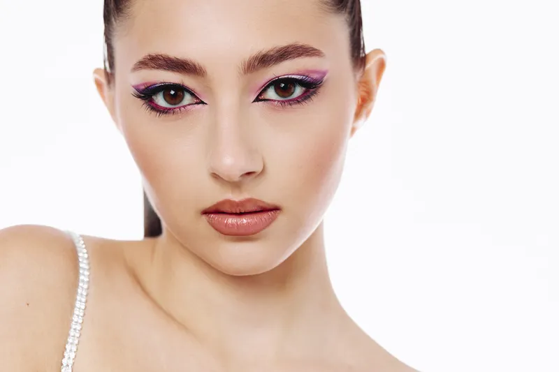 Close-up portrait of a young woman with bold creative pink eyeliner makeup and glossy lips on a white background. Fashion style, beauty expression, makeup art concept.