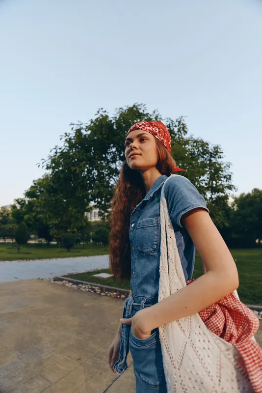 lifestyle woman wearing modern boho-western denim street style with a red bandana and tote bag, outdoors in natural light, film color effect enhancing warm tones
