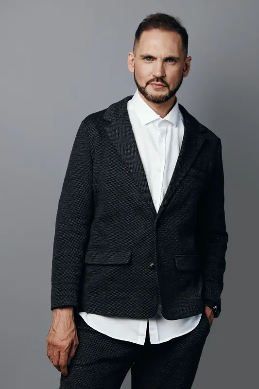 A business professional man stands against a solid colored background, radiating confidence and focus. Poised and calm, he embodies determined, executive presence.