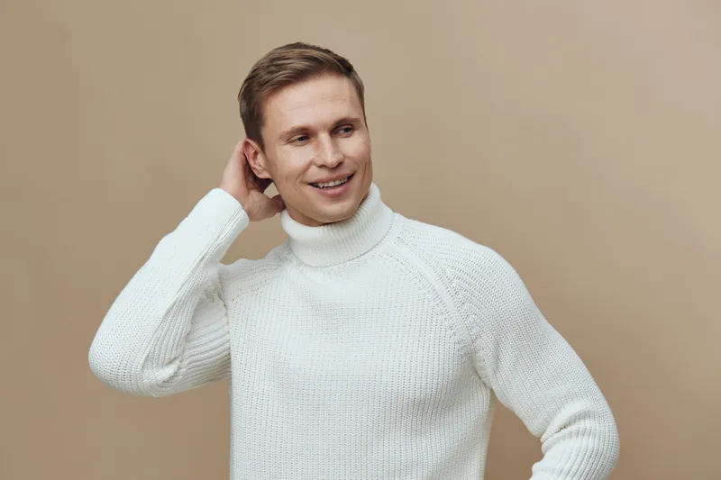 Smiling young man wearing white sweater pose indoor studio portrait isolated on beige background cheerful relaxed casual style. People lifestyle concept
