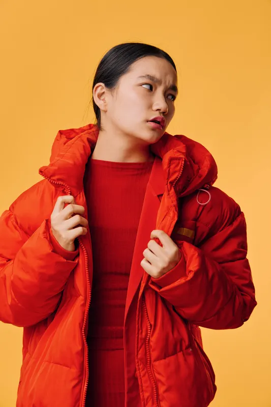 Woman in red puffer jacket and red sweater looking to side with serious expression standing against yellow background, fashion, winter style and casual outerwear concept.