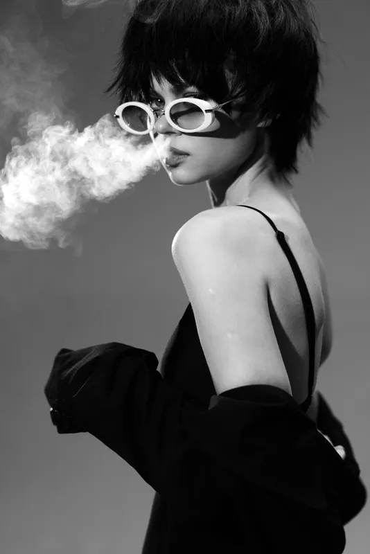 Black and white portrait of a stylish woman with sunglasses exhaling smoke in a dramatic pose