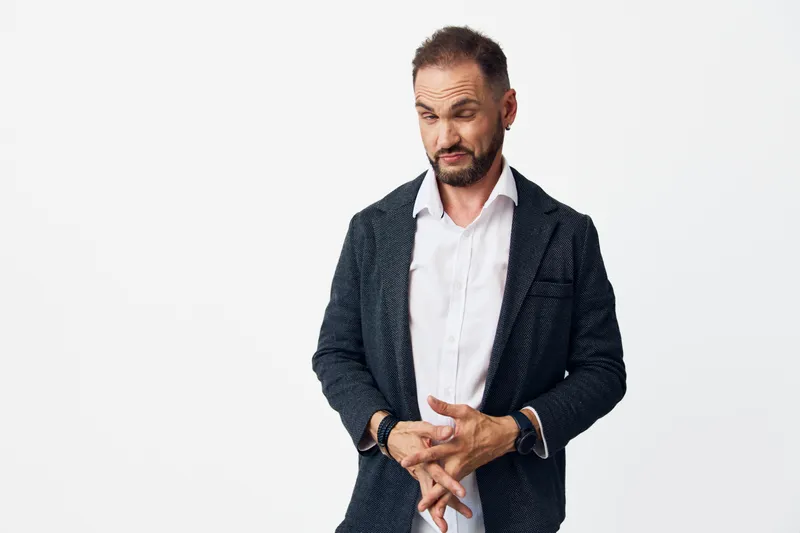 A confident business professional stands against an isolated colored background, projecting focus and calm. Wearing a blazer and white shirt, he adjusts cufflinks, ready to present ideas and lead