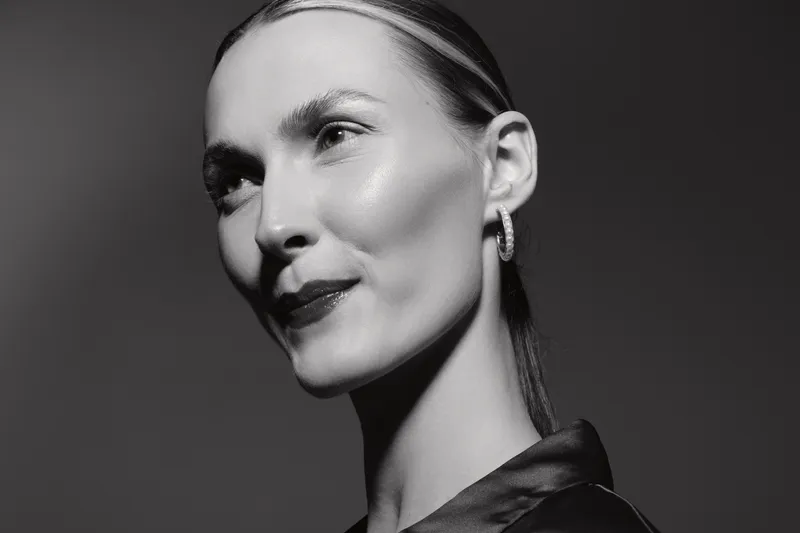 Closeup portrait of a young white woman with light skin and slicked back hair in a dark shirt. Studio lighting creates soft shadows on her face and highlights natural beauty.