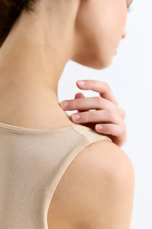 Close-up view of woman’s shoulder and neck with delicate hand touch, soft skin texture, light beige clothing, minimalistic and natural beauty concept.