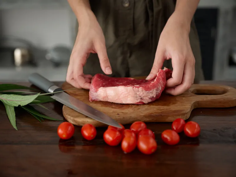Женщина с ножом в руке нарезает свежее мясо для стейка, которое будет запекаться на кухне