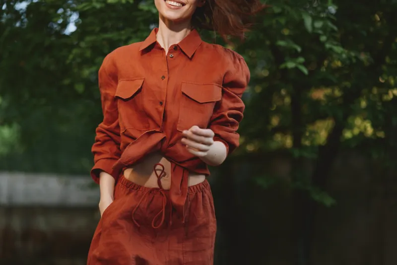 A woman in a burnt orange two piece outfit walks outdoors, exuding casual chic and a vibrant lifestyle. Sunlit scene, gentle breeze, confident, carefree mood
